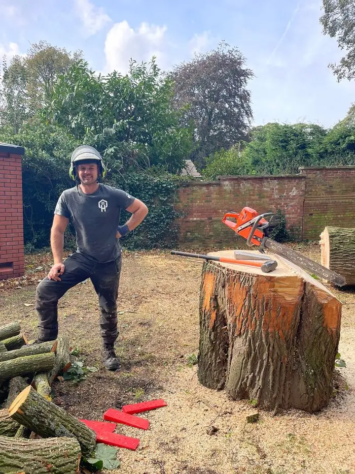 Ryan Elkin standing beside a freshly cut tree stump with a chainsaw